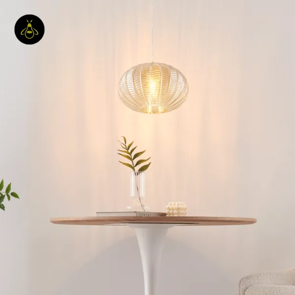 Lit textured glass pendant light above a round table with a glass vase of leaves