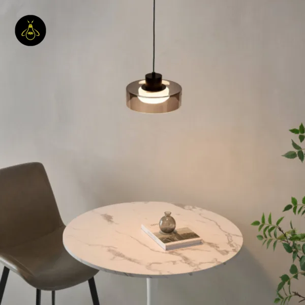 Smoked glass drum pendant light above a round marble table with a chair and plant
