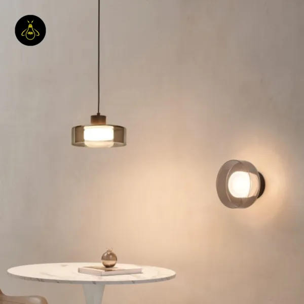 Smoked glass drum pendant light over a marble table beside a matching round wall light