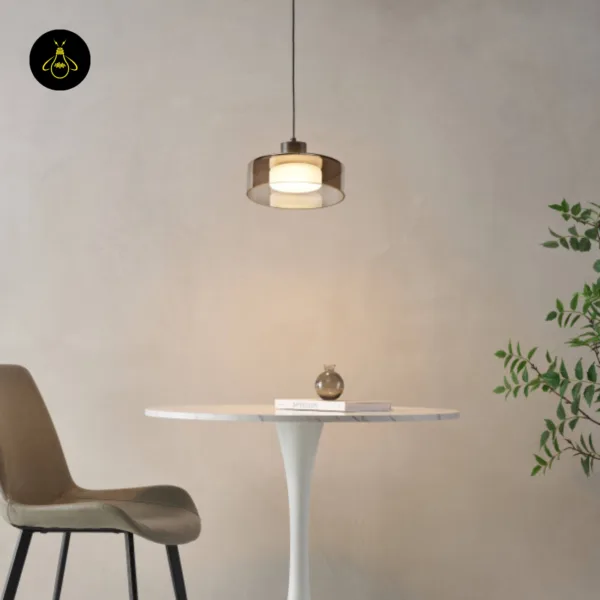 Smoked glass drum pendant light glowing warm over a round dining table