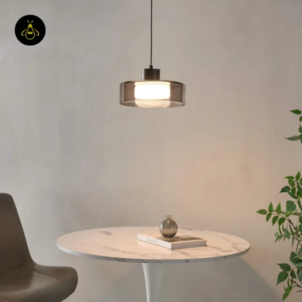 Smoked glass drum pendant light lit above a marble table with a vase and book