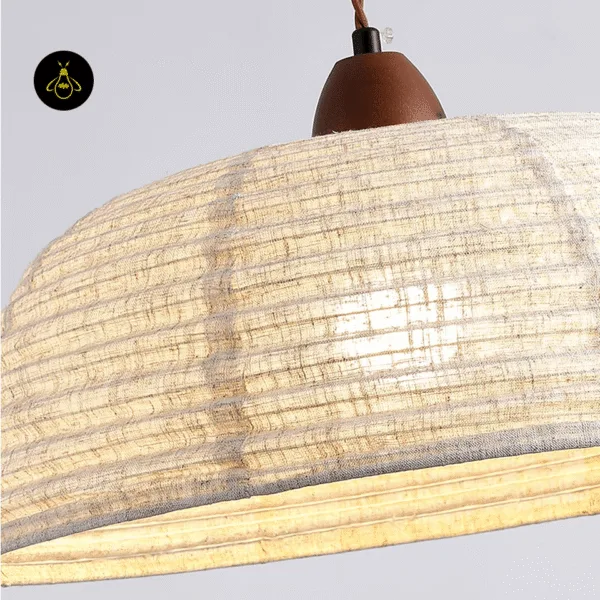 Close-up of the walnut wood cap and slubbed raw silk weave of the Japanese pendant lamp, with the bulb glowing through the silk