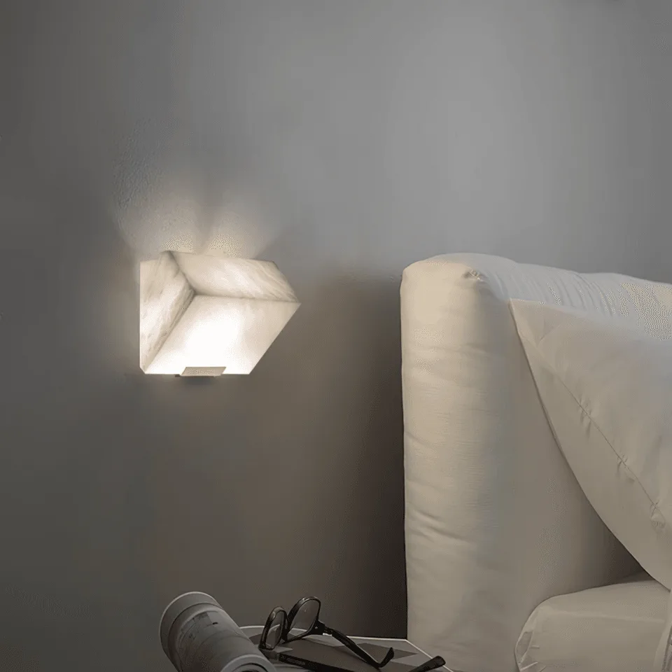 Alabaster Wall Lamp – Sculptural 15 cm Natural-Stone LED Sconce 3 Alabaster stone wall light lit beside a white upholstered bed, soft bedside light over a side table with glasses