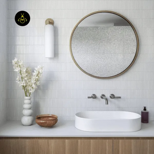 Opal cylinder glass wall light with gold cap mounted on white tile beside a round mirror and basin in a bathroom