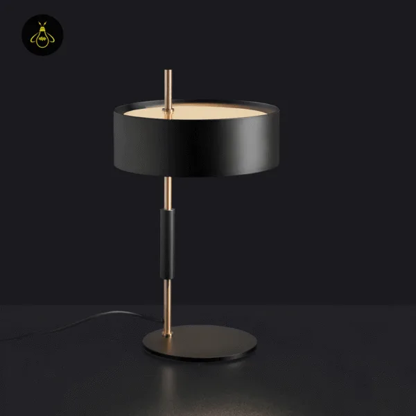 Black gold drum-shade table lamp glowing warm in a home office