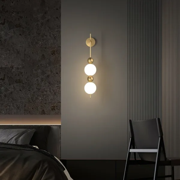 Bedside wall light glowing warm on a dark bedroom wall beside the bed and a black chair