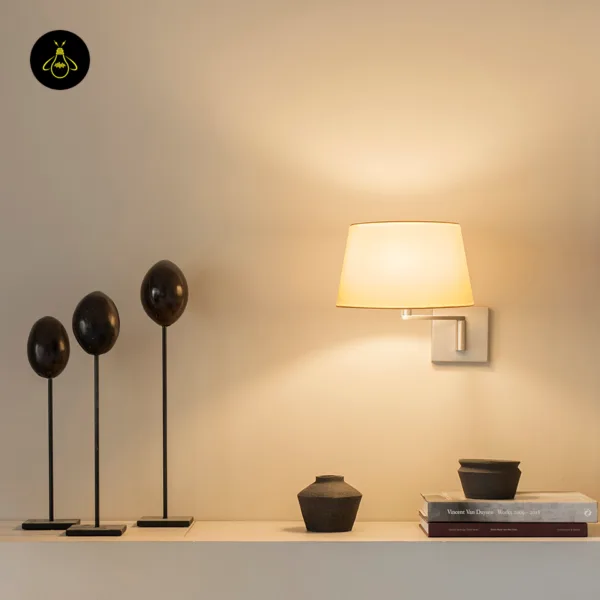 Linen swing arm wall lamp lit above a shelf with dark clay pots and books