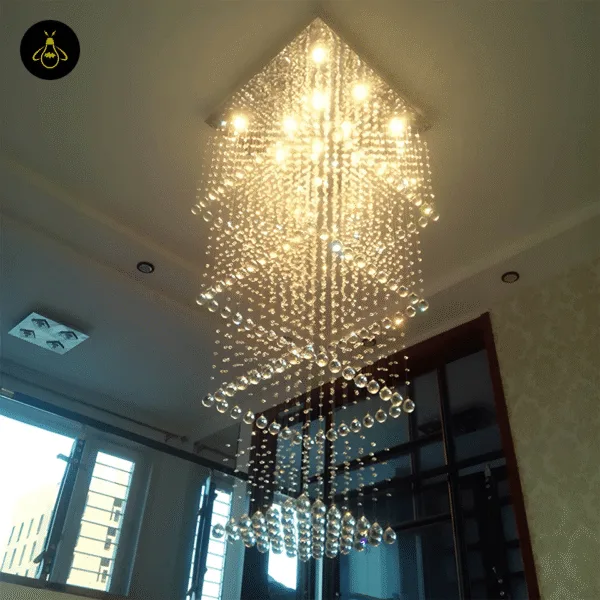 Long K9 crystal chandelier lit warm-white in a double-height entrance foyer