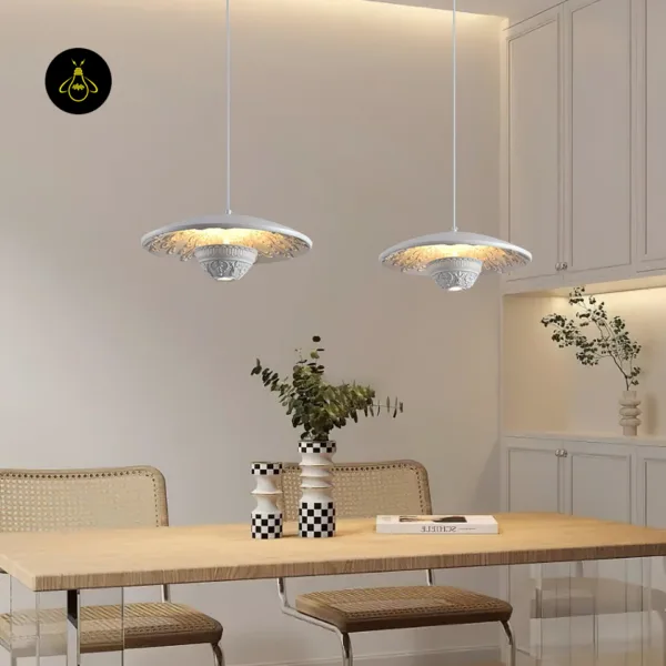 Two white pendant lights in carved resin hanging over a wooden dining table with cane chairs