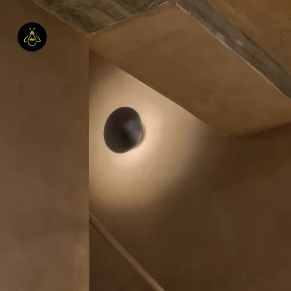 LED wall light on a stairwell wall under a concrete ceiling, warm halo on plaster
