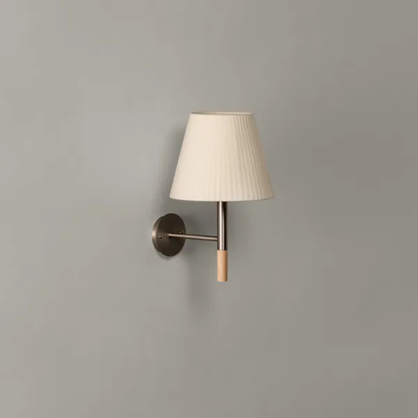 Fabric wall light switched off on a grey wall, off-white pleated silk shade, satin nickel arm and round wall plate