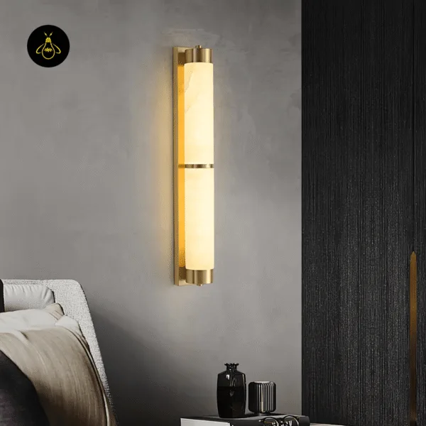 Alabaster wall light lit on a grey plaster wall beside an armchair and a black textured panel