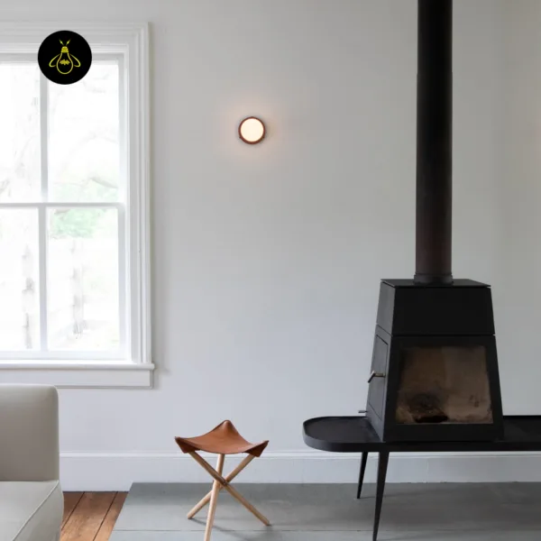 Round wall light glowing beside a window in a living room with a wood stove