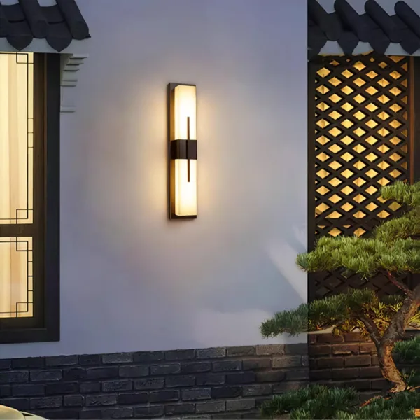 Alabaster outdoor wall light glowing on a white courtyard wall beside a lattice screen and pine
