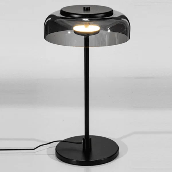 Glass table lamp with a smoked black dome shade glowing warm white on a slim stainless steel stem