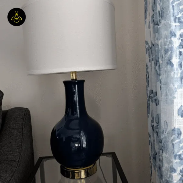 Blue ceramic table lamp on a bedside table beside floral curtains in a bedroom