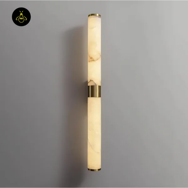Alabaster wall light lit on a grey wall, warm glow through both stone cylinders and the brushed gold band