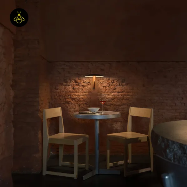 Wall light with reading light lighting a brick wall above a small table with two wooden chairs