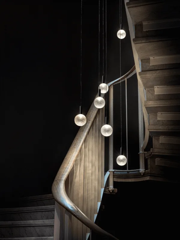 Glass sphere chandelier cascading down a curved staircase on slim black cables