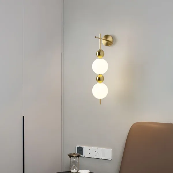 Bedside wall light lit above a small side table next to a tan sofa on a pale wall