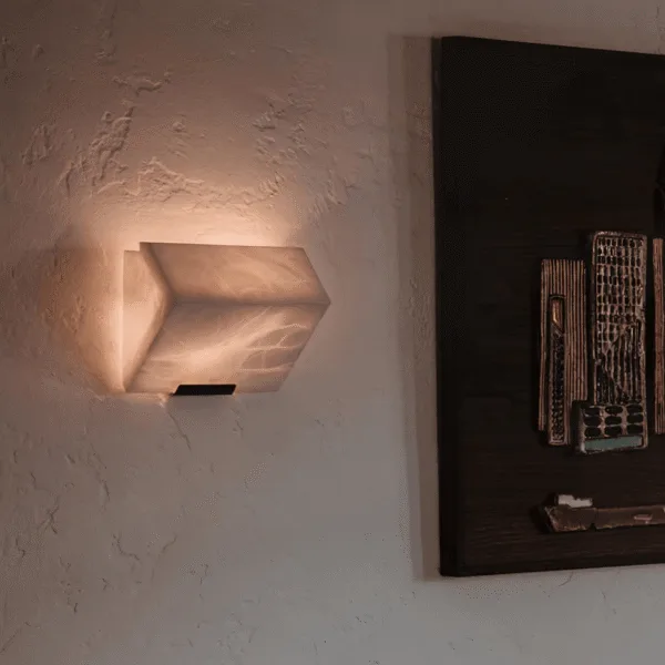 Alabaster stone wall light glowing on a textured wall beside dark framed wall art in a living room