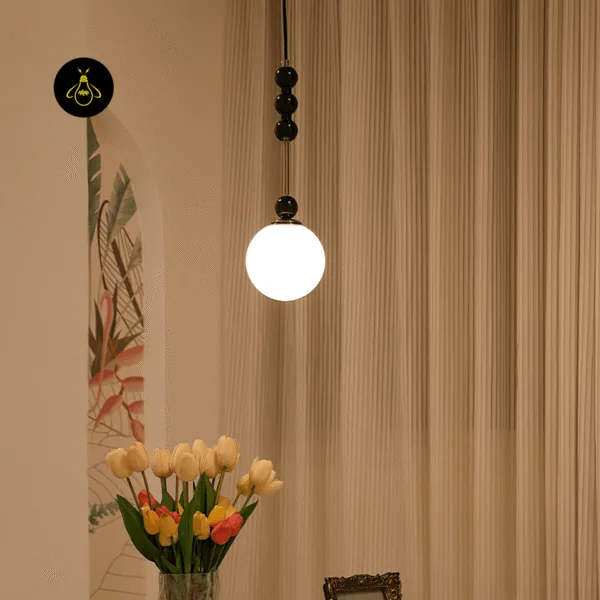 Glass globe pendant light glowing warm beside pleated beige curtains above a vase of tulips