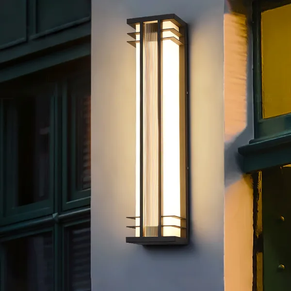 Outdoor wall sconce lit on a house facade at dusk, beside dark-framed windows