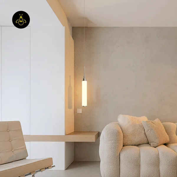 Chrome cylinder pendant light glowing in a living room corner beside a cream sofa