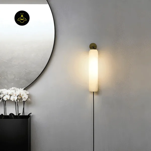 Glass wall light in a dark finish lit beside a round mirror and white orchids on a grey hallway wall