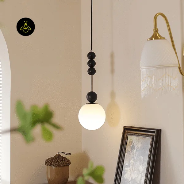 Glass globe pendant light with black beads glowing in a cream room corner beside a framed painting