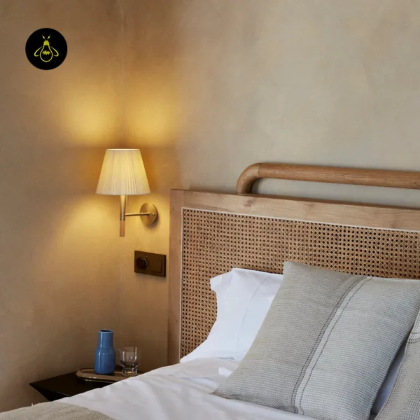Fabric wall light lit beside a cane headboard as a bedside reading light