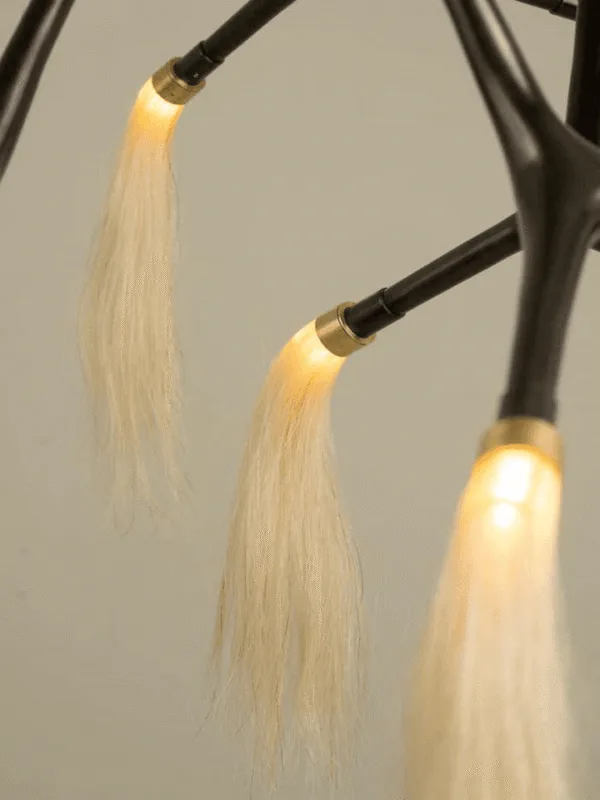 Close-up of brass ferrules and warm LEDs glowing through horsehair tassels on the bronze branch chandelier