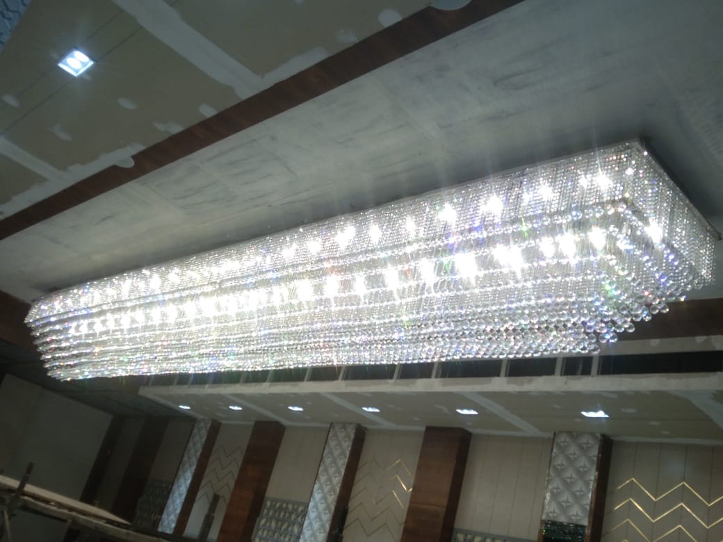 Bright rectangular crystal slab chandelier glowing above a Pune banquet interior