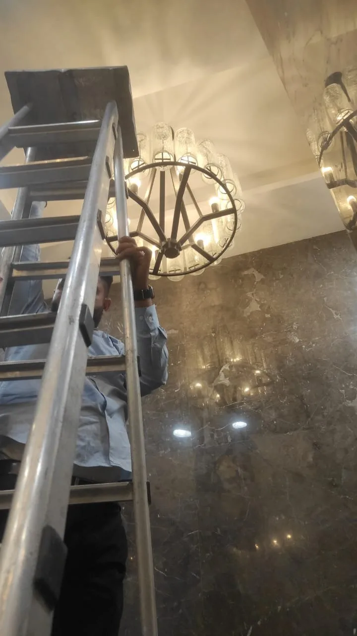 JagMag technician installing a black ring chandelier with textured glass shades in an Ace Capitol restroom