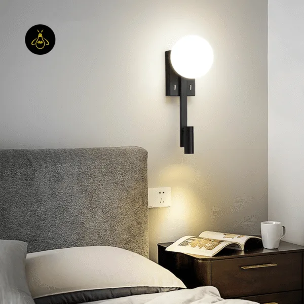 Wall mounted study lamp beside a bed and bedside table with an open book, opal globe lit
