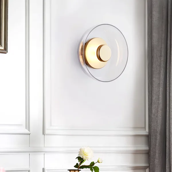 Circular wall light on a white panelled wall, clear glass dish and brass-finish disc