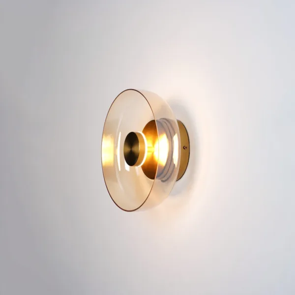 Circular wall light switched on, warm 3000K glow behind a tinted glass dish and brass-finish disc, side view