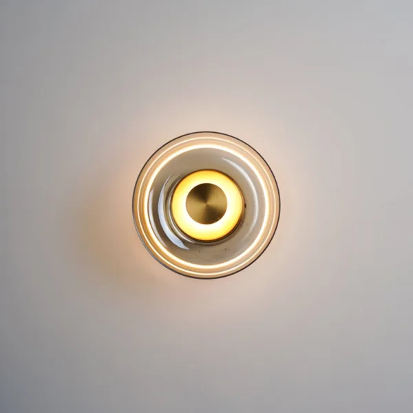 Circular wall light lit, front view, warm halo ring on the glass dish around a brass-finish disc