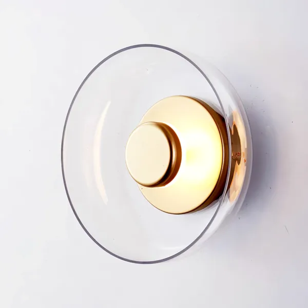 Clear borosilicate glass dish of the circular wall light around a glowing brass-finish disc, angled view
