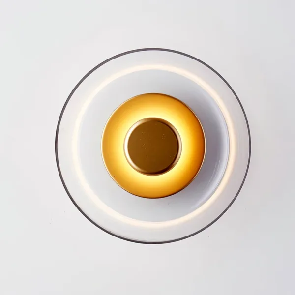 Circular wall light seen head-on, glowing brass-finish disc inside a clear glass dish with a halo on the rim