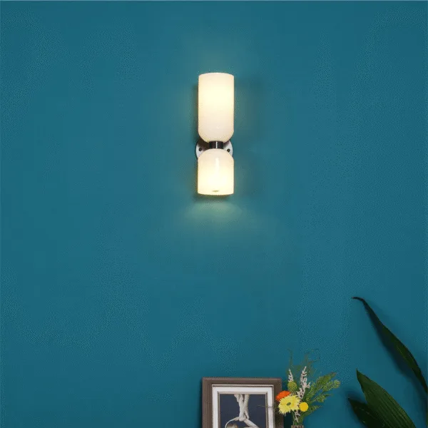 Lit wall sconce for bedroom with opal borosilicate glass shades on a teal wall above a picture frame