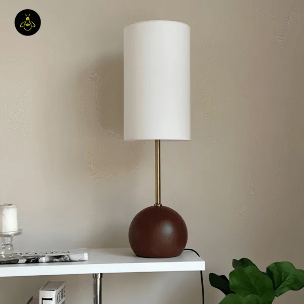 White fabric shade of the wooden sphere table lamp casting warm light on a bedside table