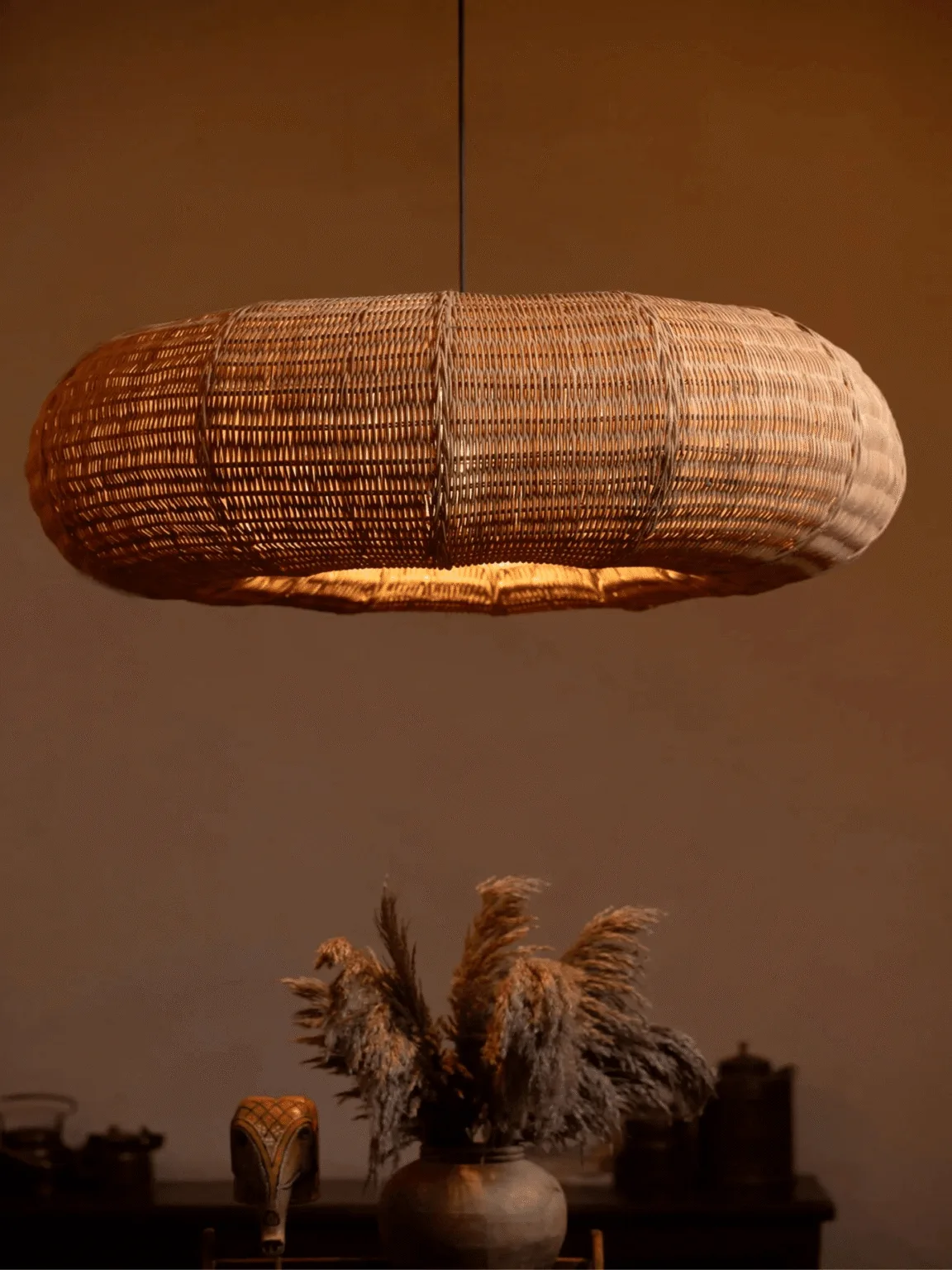 Rattan hanging light with a wide handwoven cane shade glowing warm over a boho living space