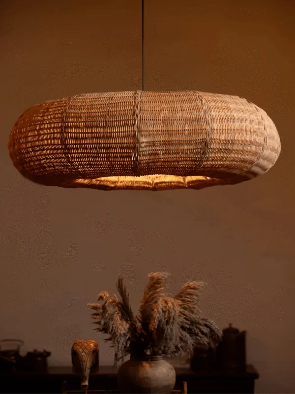 Cane frame pendant light glowing warm over a dark sideboard with dried pampas grass in a clay pot