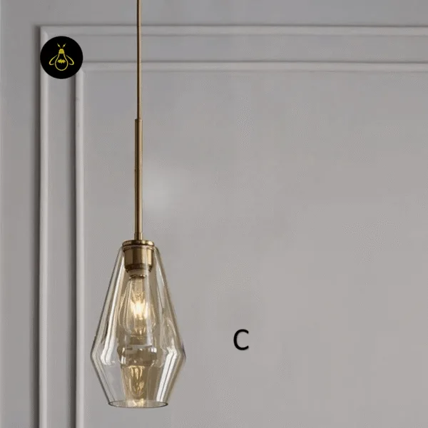 Amber glass pendant light size C, Ø 17 cm tall faceted shade on a brass-finish rod against a grey panelled wall