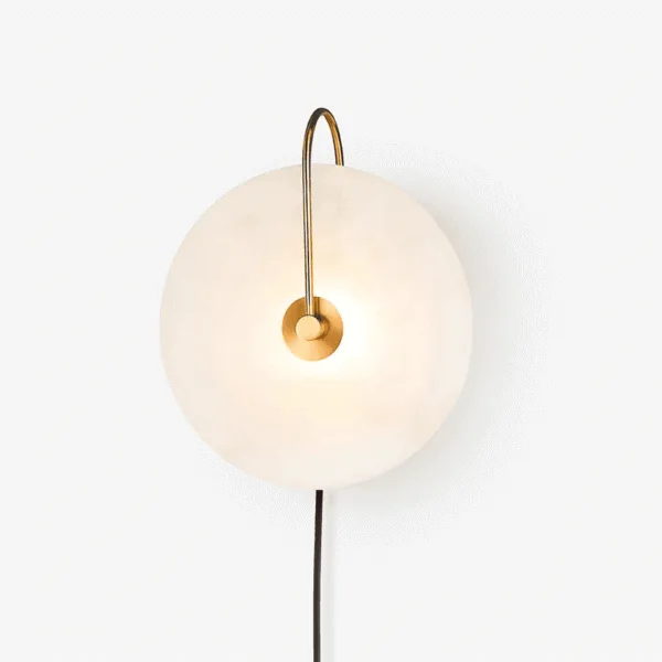 Gold plug in wall lamp, front view of the round alabaster disc and curved arm with its black cord