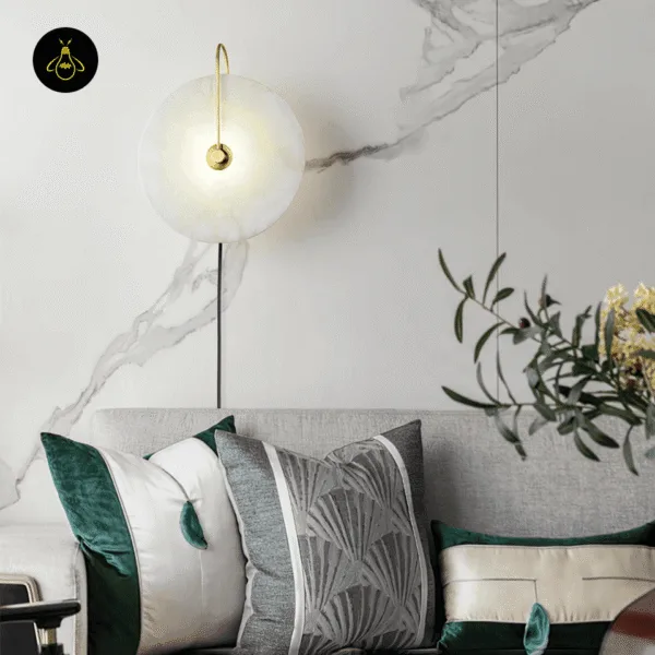 Gold plug in wall lamp above a grey sofa against a marble-veined wall in a living room