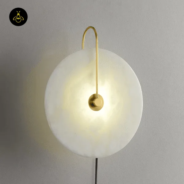 Gold plug in wall lamp lit on a grey wall, warm light glowing through the alabaster disc