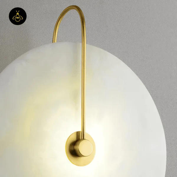 Close-up of the gold arm and centre boss on the lit alabaster disc of the plug in wall lamp