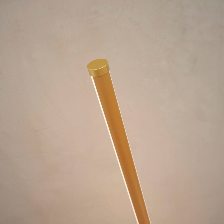 Gold LED floor lamp lighting a bedroom corner beside a bed